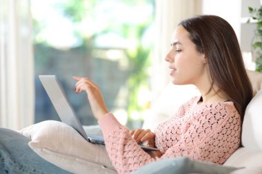 Evde oturan bir kadının yan görünüm portresi dizüstü bilgisayar kullanıyor.