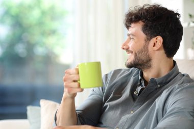 Evdeki kanepede oturup pencereden kahve içen mutlu bir adamın profili.