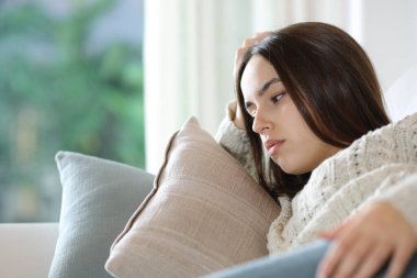 Endişeli bir kadın kanepeye uzanıp evine bakıyor.