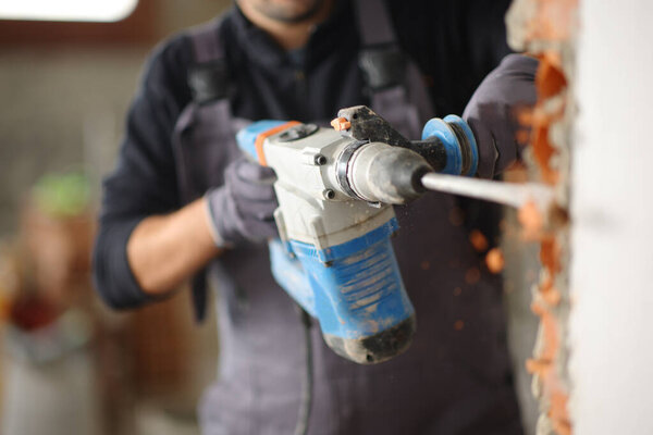 Close up of a construction worker using rotary hammer to wreck wall in a house under renovation