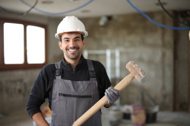Tadilat altındaki bir evde poz veren mutlu bir inşaat işçisinin portresi.