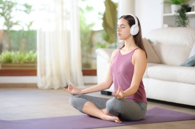 Yogi evde kulaklık takarak yoga egzersizi yapıyor.