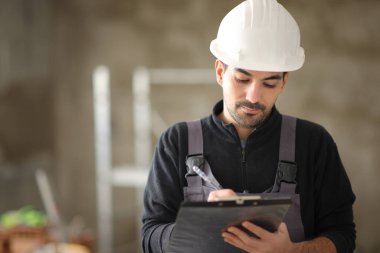 Bir inşaat işçisinin portresi. Evdeki panoya not alıyor.