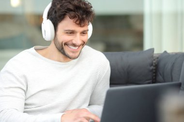 Kulaklıklı mutlu adam evdeki terasta dizüstü bilgisayarı izliyor.