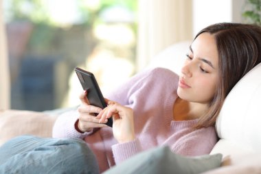 Evdeki koltukta oturan akıllı telefonu kullanan ciddi bir kadın.