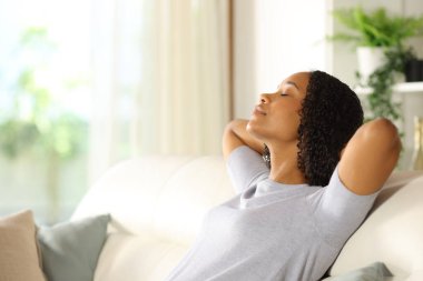 Evdeki kanepede oturup dinlenen siyah bir kadının profili.