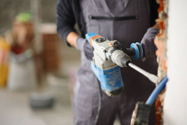 Close up of a construction worker hands using rotary hammer to wreck a wall in a house under renovation