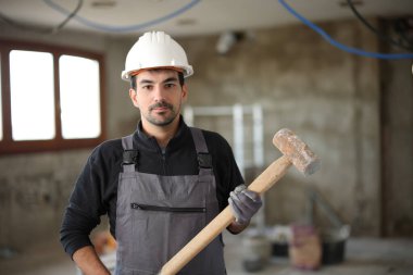 Reform altındaki bir evde çekiçle poz veren ciddi bir inşaat işçisinin portresi.