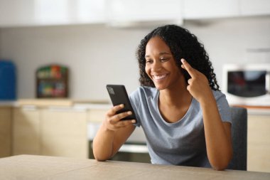 Mutlu siyahi kadın parmaklarını çapraz yapıp mutfaktaki telefonu kontrol ediyor.