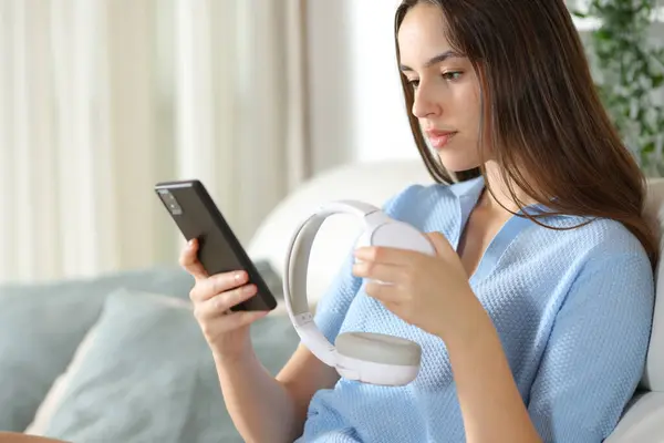 stock image Woman pairing headphone with smart phone sitting at home