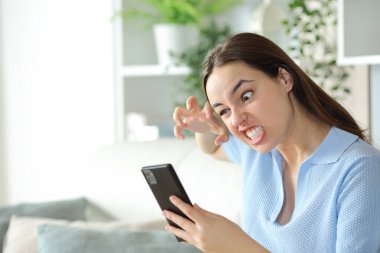Öfkeli kadın evde cep telefonunu kontrol ediyor.
