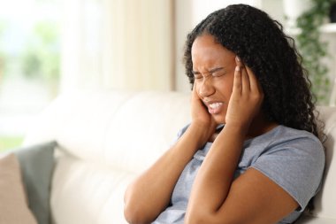 Siyahi kadın evde oturup migren ağrısı çekiyor.