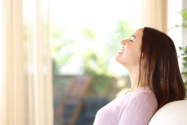 Lüks bir evde, koltukta oturmuş temiz hava soluyan mutlu bir kadının yan görüntüsü.