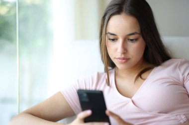 Evdeki koltukta oturan akıllı telefonu kullanan ciddi bir kadın.