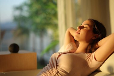 Evdeki koltukta oturan ve arka planda akıllı konuşan bir kadın.