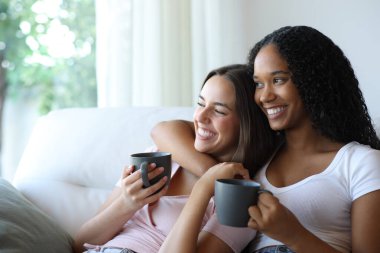 Kahve içen mutlu ırklar arası lezbiyen çift evlerinin penceresinden dışarı bakıyor.