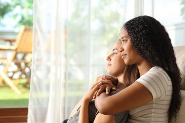 Rahatlamış lezbiyen ırklar arası bir çift pencereden dışarı bakıyor. Evde yerde oturuyor.