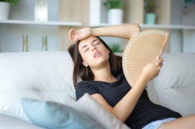 Stresli bir kadın sıcak bir yaz günü evde bir kanepede oturup yellenir.