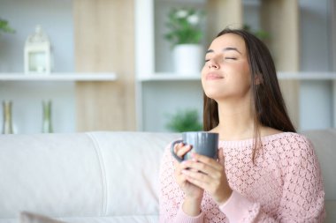 Kadın rahatlıyor, kahve içiyor ve temiz hava soluyor evdeki koltukta oturuyor.