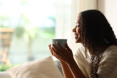 Arka planda mutlu, siyah bir kadının kahve içerken camdan içeri baktığı görülüyor.