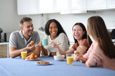Mutlu ırklar arası oda arkadaşları ve arkadaşları kahvaltıda mutfakta konuşuyor ve gülüyor.