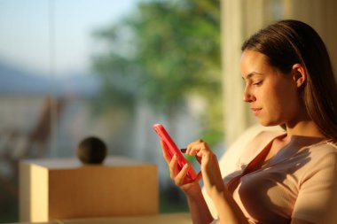 Gün batımında akıllı hoparlörleri kontrol etmek için telefonu kullanan ciddi bir kadın.