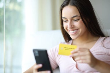 Evde kredi kartı ve akıllı telefon kullanan mutlu bir kadın.