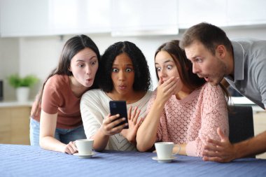 Dört tane şok olmuş ırklar arası arkadaş mutfaktaki telefonu kontrol ediyor.