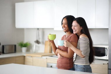 Evdeki mutfakta kahve içen mutlu ırklar arası lezbiyen çift.