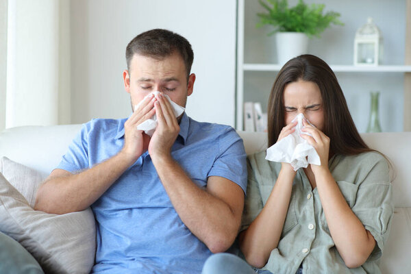 Ill couple suffering influenza blowing on tissue sitting on a couch at home