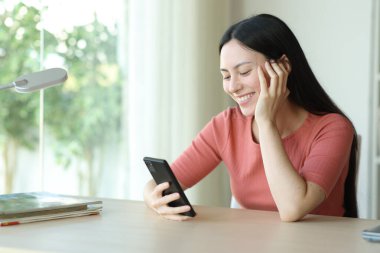 Mutlu Asyalı kadın evdeki masada akıllı telefonu kontrol ediyor.