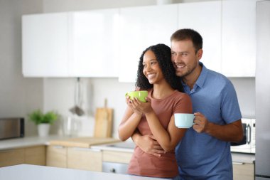 Mutlu ırklar arası bir çift mutfakta duruyor ve evde kahve içip sarılıyorlar.