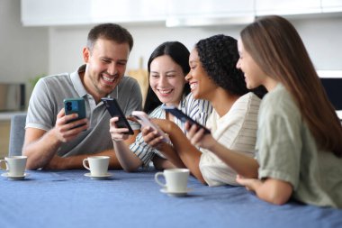 Dört mutlu ırklar arası arkadaş mutfakta durup evdeki telefonları kontrol ediyor.