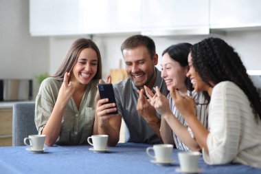 Dört mutlu ırklar arası arkadaş evdeki mutfakta telefonlarını kontrol ediyor.