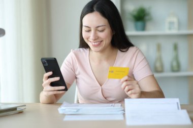Akıllı telefon ve kredi kartıyla faturaları ödeyen mutlu Asyalı kadın.
