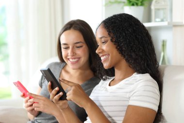 Mutlu ırklar arası ev arkadaşları evdeki bir kanepede akıllı telefonlarını kontrol ediyor.