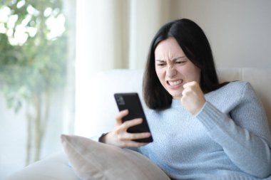 Kızgın Asyalı kadın evde rahatsız edici telefon içeriğini kontrol ediyor.