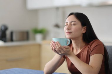 Asyalı kadın evde kahve ya da çay içerek rahatlıyor.
