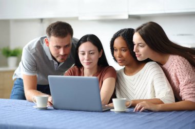 Dört ciddi ırklar arası arkadaş evdeki mutfakta dizüstü bilgisayar kullanıyor.