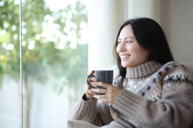 Mutlu Asyalı kadın evdeki kanepede oturup çay içiyor.