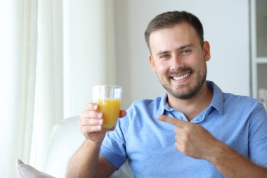 Mutlu adam portakal suyu bardağını gösteriyor ve sana bakıyor.