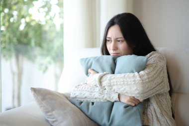 Üzgün Asyalı kadın evdeki kanepede oturup yastığa sarılmaktan şikayetçi.