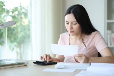 Ciddi Asyalı kadın faturaları evde kontrol ediyor.