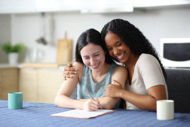 Mutlu ırklar arası lezbiyen çift evdeki mutfakta kontrat imzalıyor.