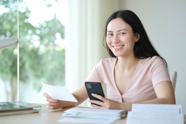 Fatura ve telefon taşıyan Asyalı kadın evde sana bakıyor.