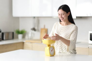 Mutlu Asyalı kadın evdeki mutfakta tartıyla yemek tartıyor.