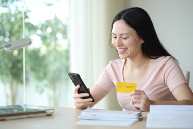 İnternette kredi kartı ve cep telefonuyla faturaları ödeyen mutlu Asyalı kadın.