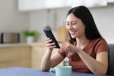 Mutfakta cep telefonu kullanan mutlu Asyalı kadın.
