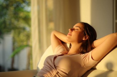 Gün batımında evinde kanepede oturan bir kadın. 