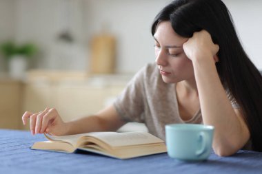 Evdeki mutfakta kitap okuyan konsantre Asyalı kadın.